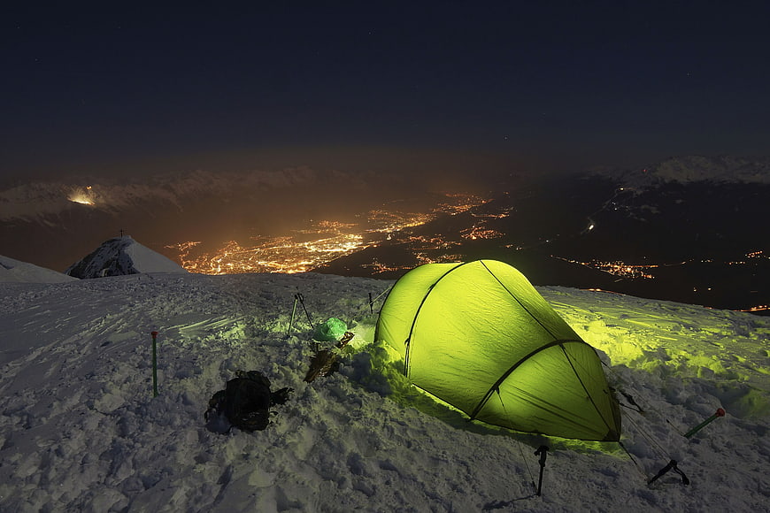 Glowing Green Tent on Snowy Mountain Peak at Night