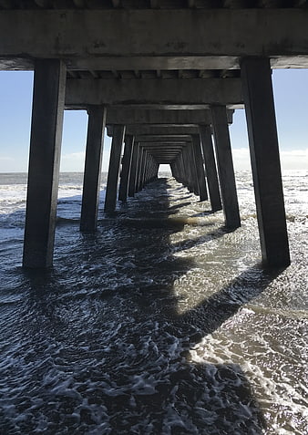 Perspective view under concrete pier pillars with ocean waves