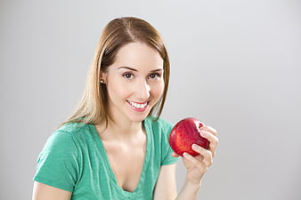 Smiling woman holding red apple against gray background