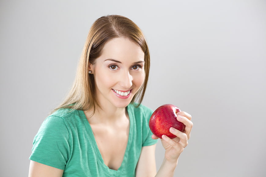 Smiling woman holding red apple against gray background