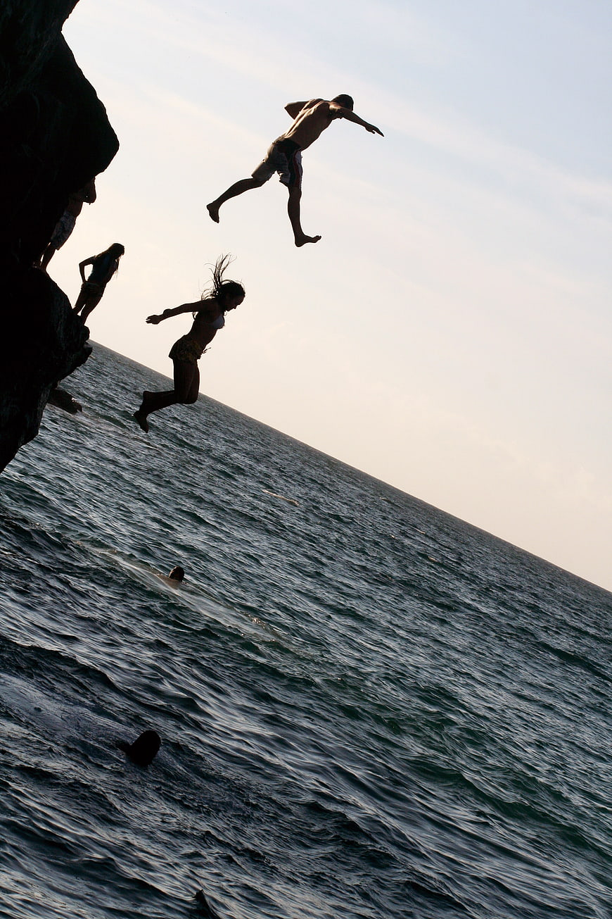 Silhouettes of People Cliff Diving into the Ocean