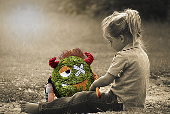 Toddler girl sitting outdoors with green monster plush toy
