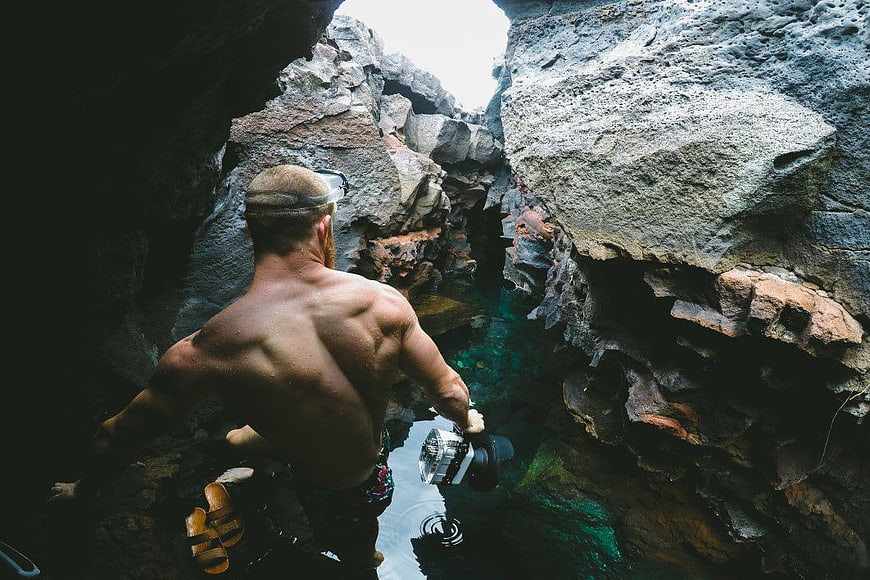 Man with Camera Exploring Rocky Cave Pool