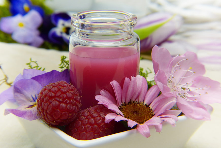 Raspberry juice in glass jar with fresh berries and pink flowers