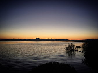 Serene Lake Sunset with Silhouetted Mountains and Wind Turbines