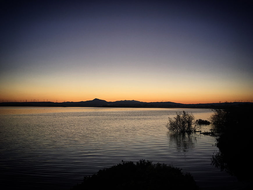 Serene Lake Sunset with Silhouetted Mountains and Wind Turbines