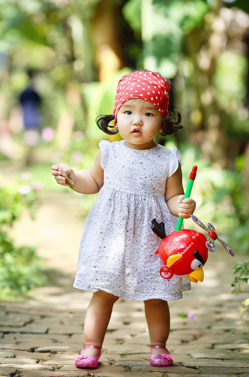 Cute toddler girl with red toy in garden