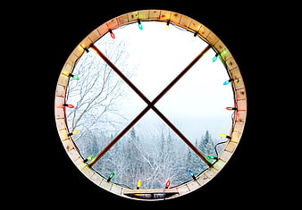 Round window with Christmas lights framing snowy winter forest view