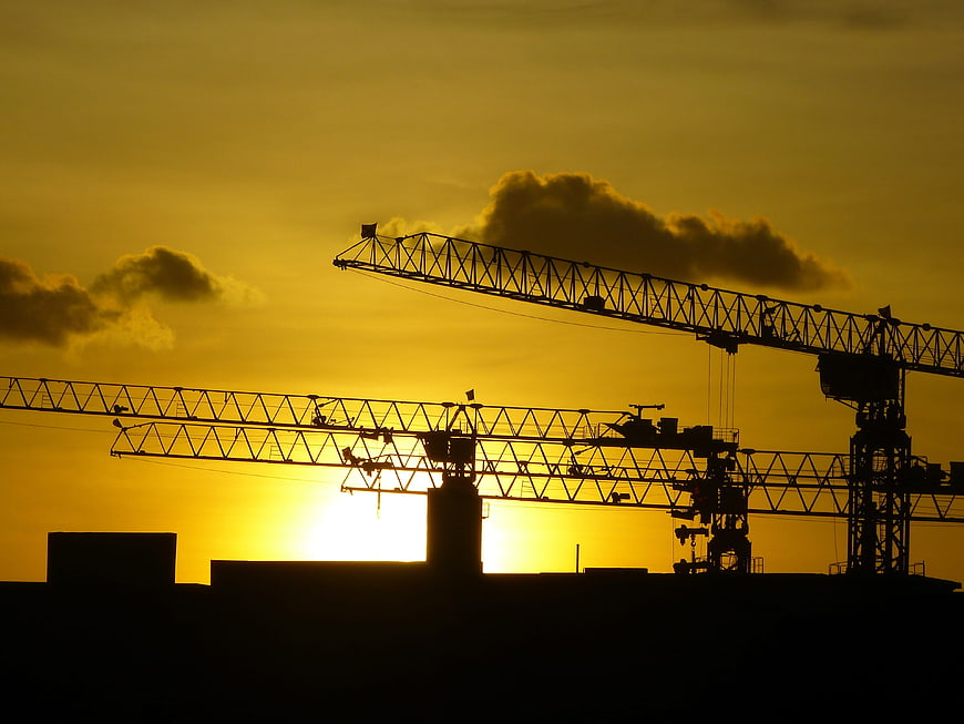 Construction Cranes Silhouette Against Golden Sunset Sky