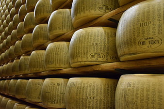 Rows of aging Parmigiano Reggiano cheese wheels on wooden shelves