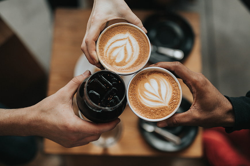 Friends toasting with latte art and iced coffee in a cafe