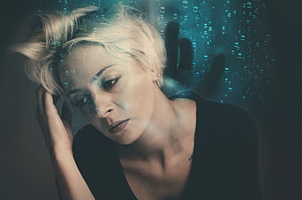 Pensive blonde woman behind rain-streaked glass