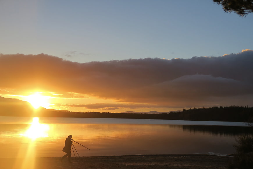 Silhouette of photographer with tripod at lake sunset
