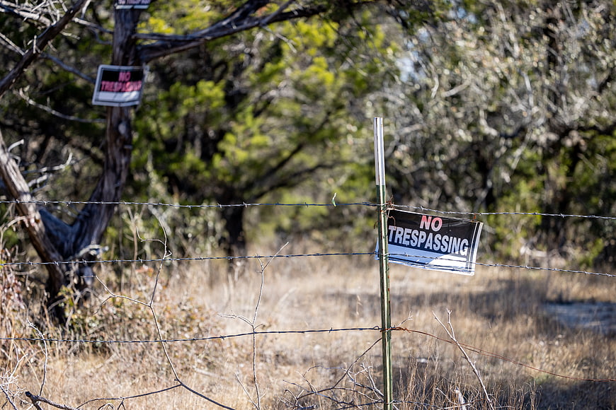 No Trespassing Sign on Barbed Wire Fence in Dry Field