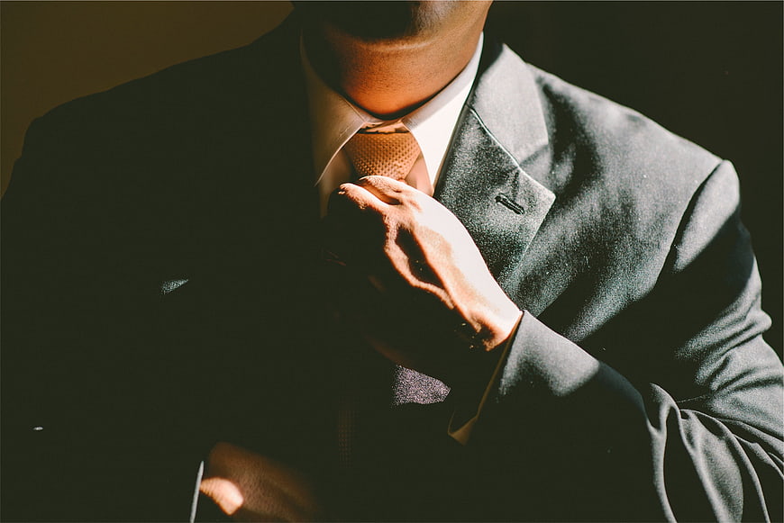 Man adjusting tie in dark suit with dramatic lighting