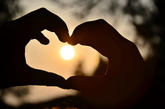 Silhouette of Hands Making Heart Shape Around Sunset Sun