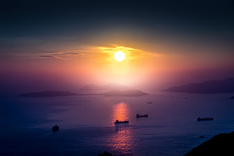 Sunset over Hong Kong harbor with cargo ships and distant mountains