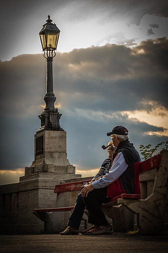 Senior couple sitting on bench under street lamp at sunset