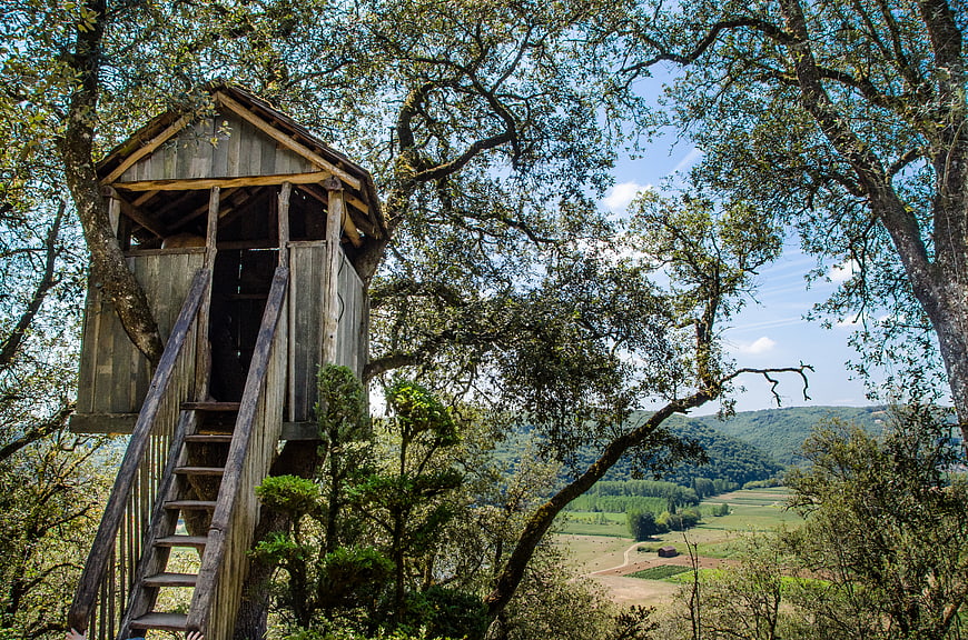Rustic wooden treehouse with stairs overlooking green valley