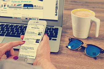 Woman reading news on smartphone with coffee and laptop
