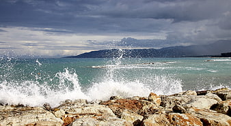 Dramatic ocean waves crashing against rocky coastline under stormy sky