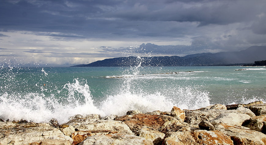 Dramatic ocean waves crashing against rocky coastline under stormy sky