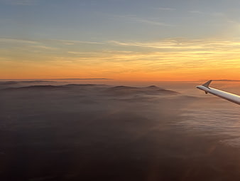 Airplane wing over sea of clouds at sunset
