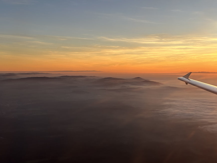Airplane wing over sea of clouds at sunset