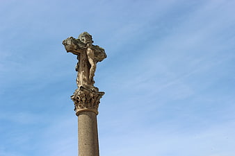 Stone Crucifix Statue on Column Against Blue Sky