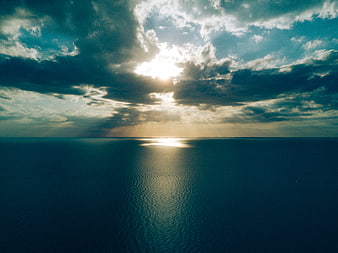 Dramatic Sunlight Breaking Through Clouds Over Calm Ocean Horizon