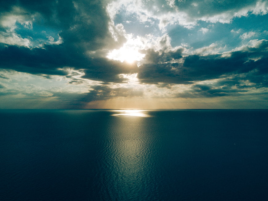 Dramatic Sunlight Breaking Through Clouds Over Calm Ocean Horizon