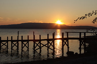 Silhouetted wooden pier at sunset over calm lake