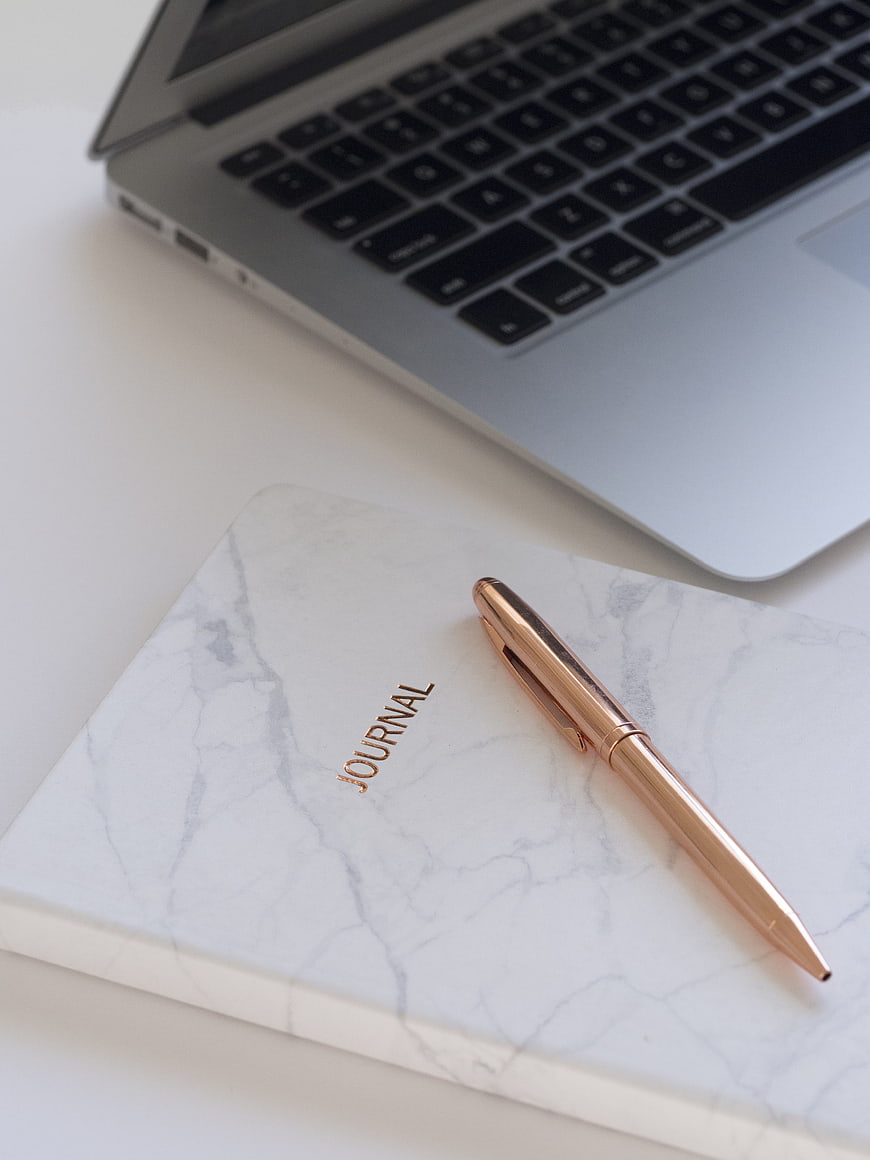 Rose gold pen on marble journal with laptop