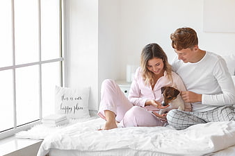 Happy couple in pajamas playing with dog on bed