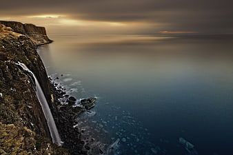 Dramatic waterfall cascading down rugged cliff to misty ocean