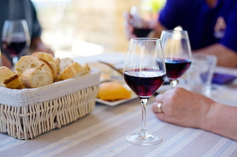 Red wine glasses and bread basket on a table with people dining