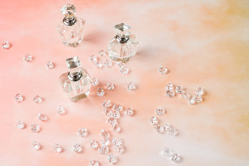 Crystal perfume bottles and gems on pastel pink background