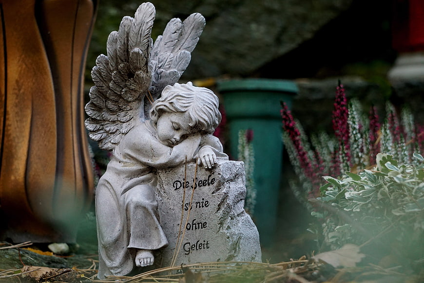 Grieving Angel Statue On Stone Tombstone In Garden