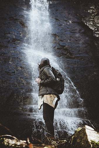 Hiker with Backpack Standing in Front of Waterfall