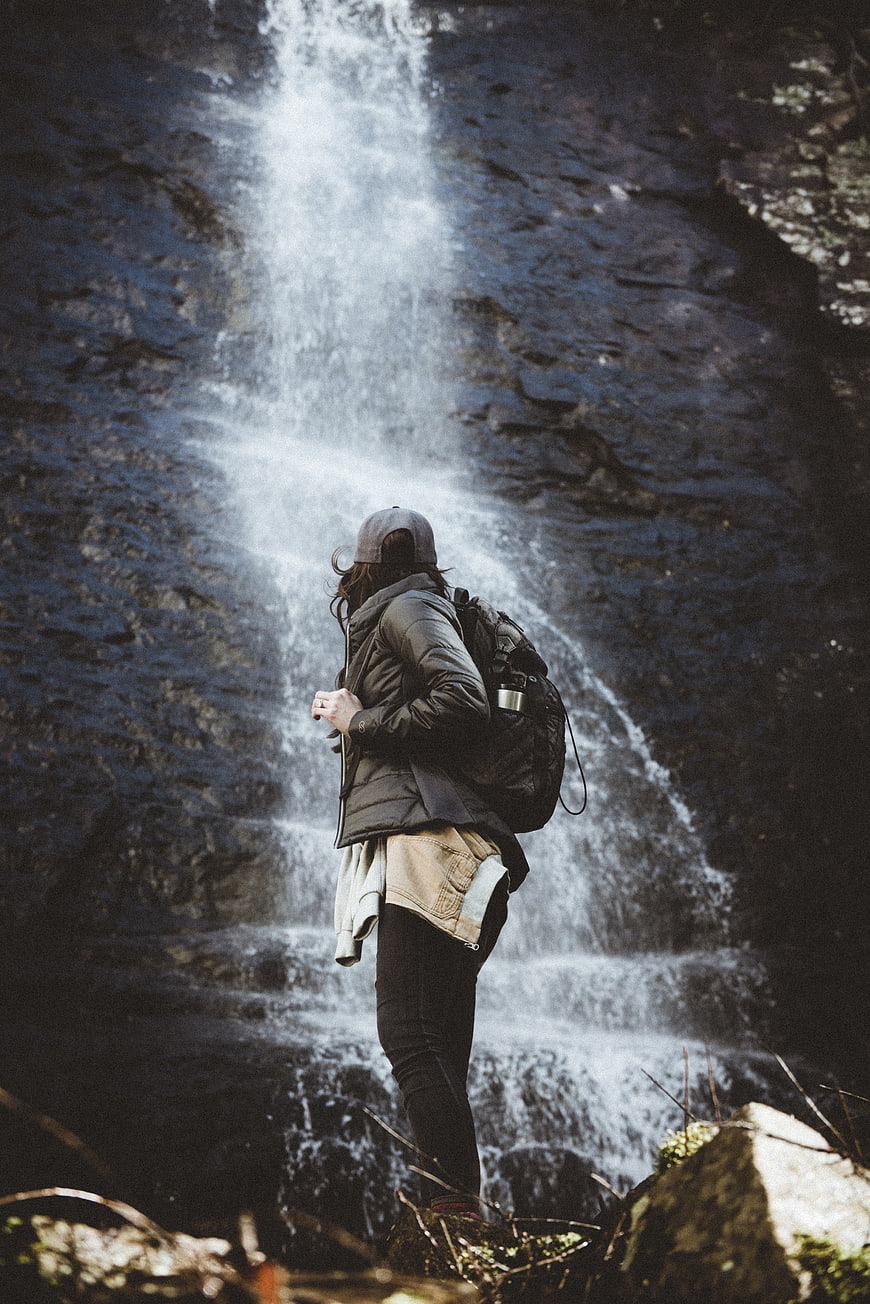 Hiker with Backpack Standing in Front of Waterfall