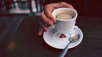 Hand holding white espresso cup on dark wooden table