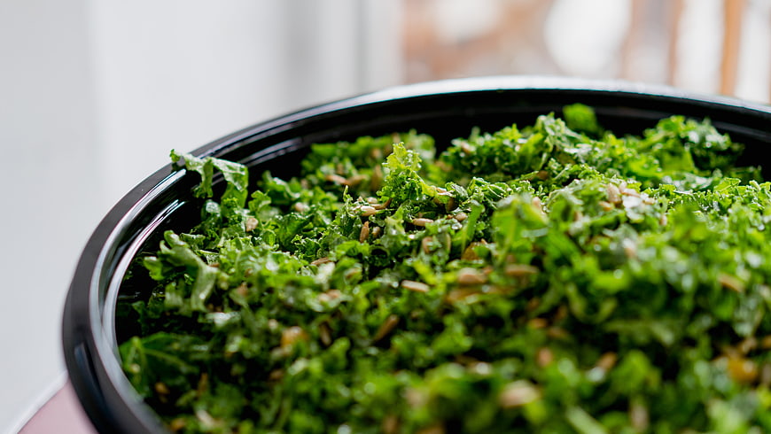 Close-up of fresh kale salad with seeds in a black bowl