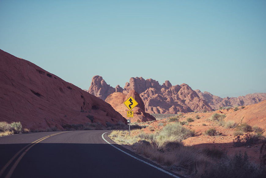 Winding Desert Road with Red Rock Formations and Sign
