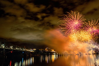 Colorful fireworks exploding over river and bridge at night