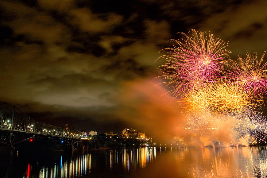 Colorful fireworks exploding over river and bridge at night