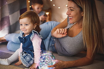 Happy mother and toddler playing with fairy lights in a cozy indoor tent