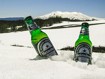Two Heineken beer bottles in snow with mountain background
