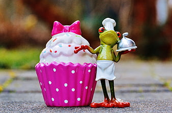 Cute frog chef figurine presenting a pink cupcake