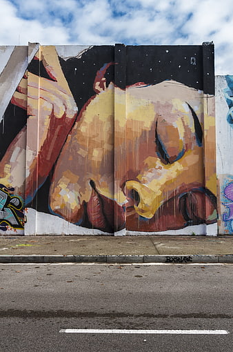 Large urban street art mural of a sleeping face on a wall
