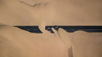Aerial view of car on desert road partially covered by sand